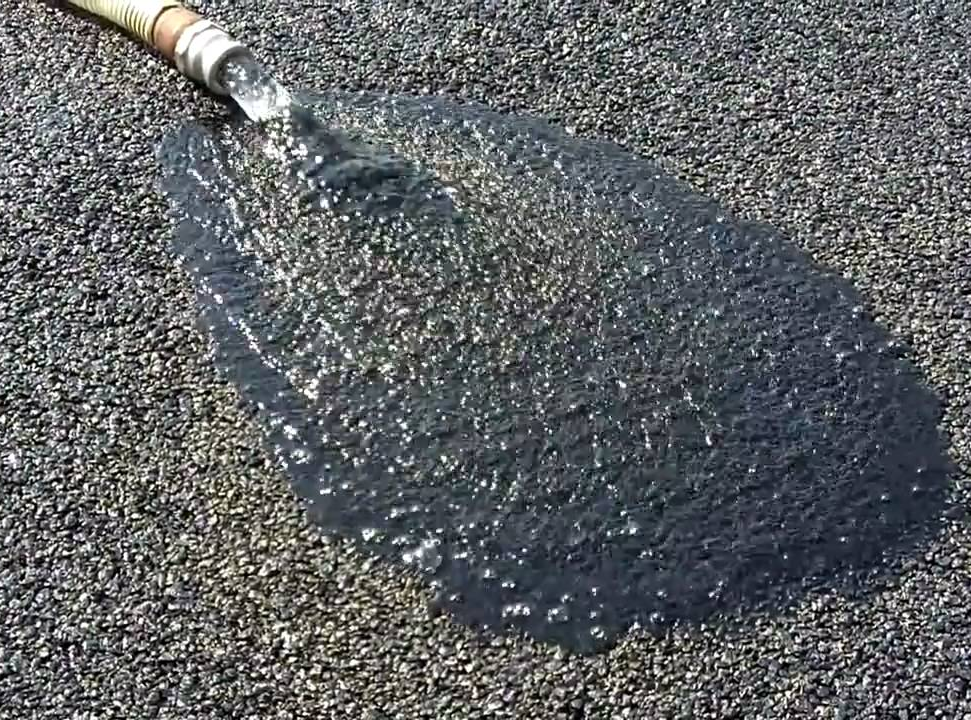 hose poring water on porous asphalt to demonstrate the ability for porous asphalt to drain.